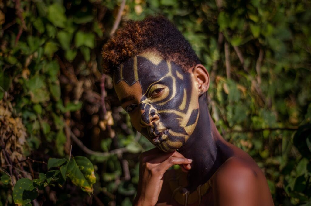 Close-up portrait of a person with artistic face paint surrounded by lush greenery.